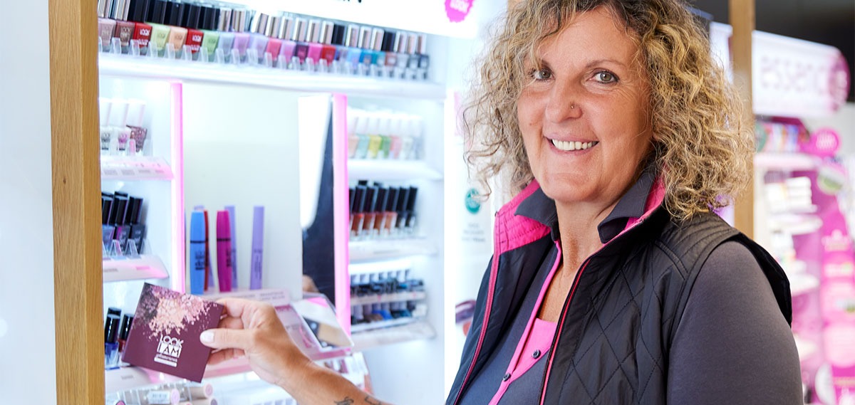 Eine lächelnde Mitarbeiterin zeigt eine Lidschattenpalette.