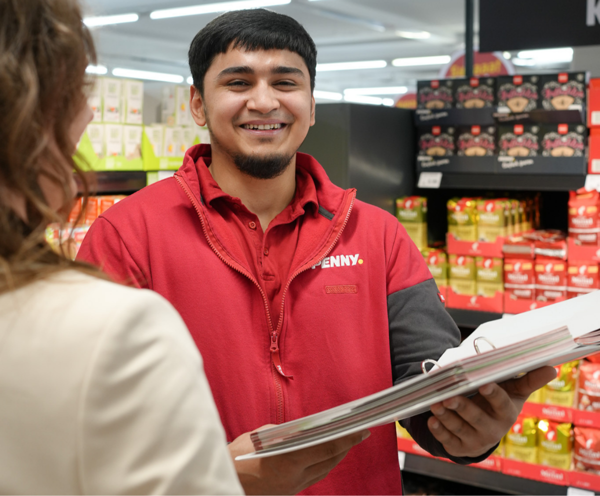 Ein lächelnder Lehrling vor einem Regal.