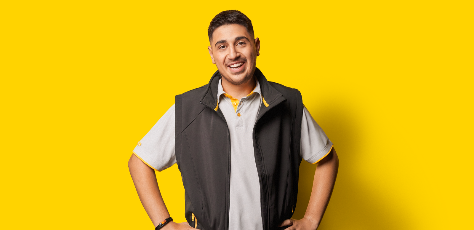 Ein Mitarbeiter steht lächelnd vor einer gelben Wand.
