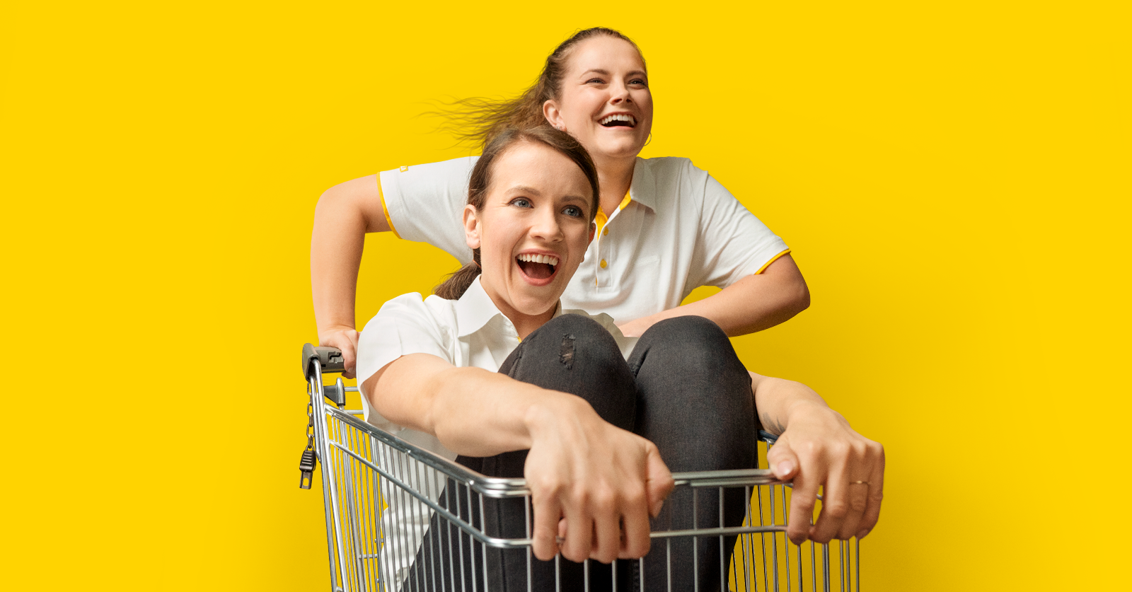 Zwei Mitarbeitende haben Spaß mit einem Einkaufswagen.
