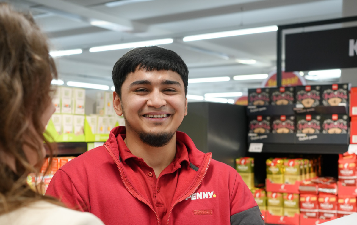 Ein lächelnder Lehrling vor einem Regal.