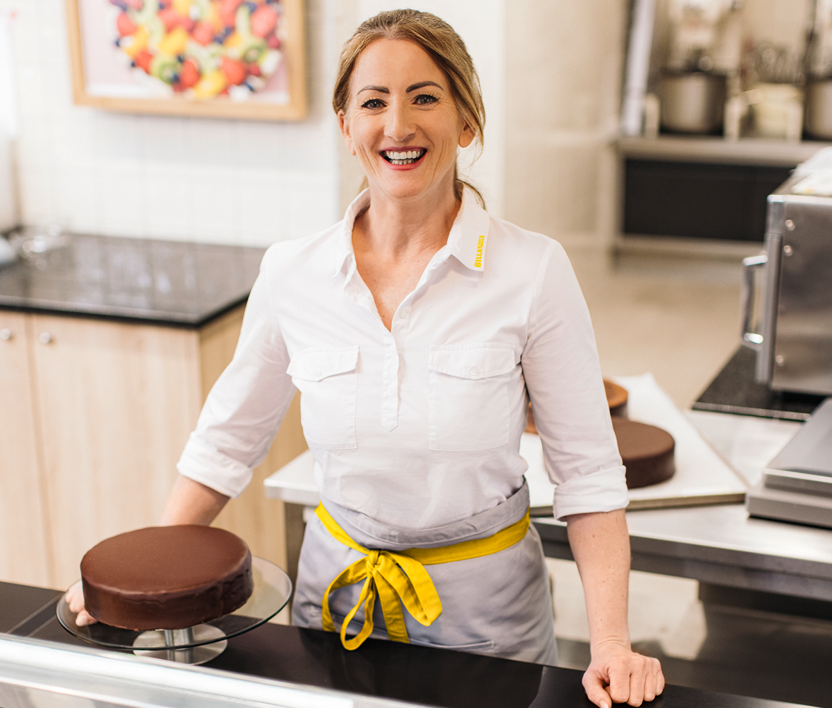 Eine lachende Mitarbeiterin steht vor einem Kuchen.